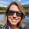 Woman with long blonde hair and sunglasses standing outside near lake.