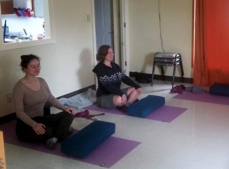Two women sit cross legged, practising yoga. 