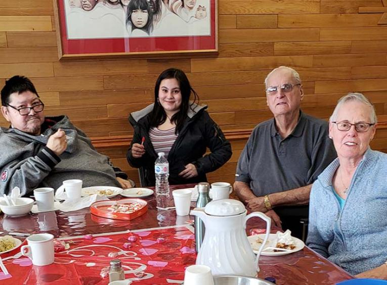 Two men and two women enjoy a meal and look into the camera.