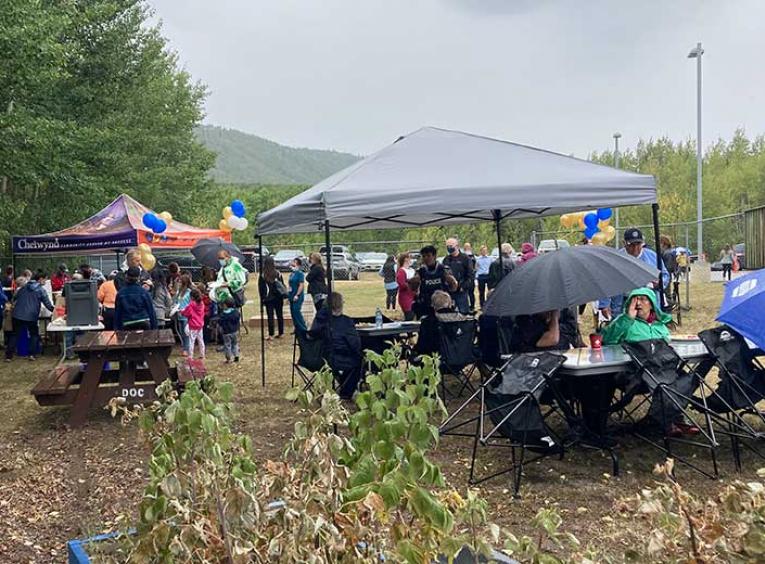 Group of people gathered outside under tents in the rain