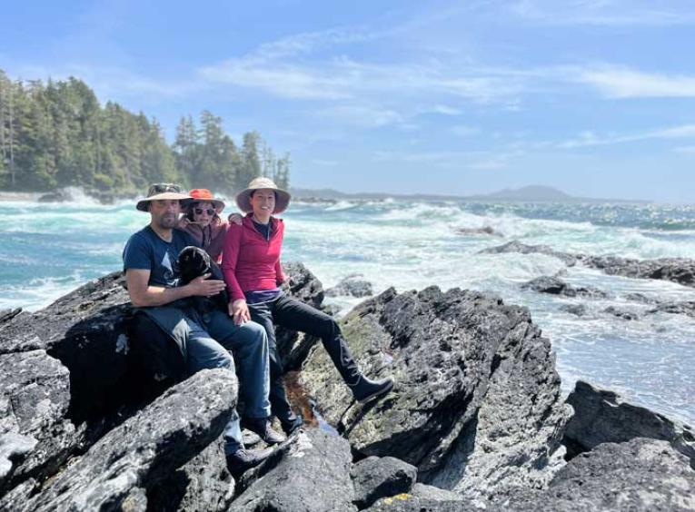A family sits on a pile of rocks near the ocean with a blue sky.