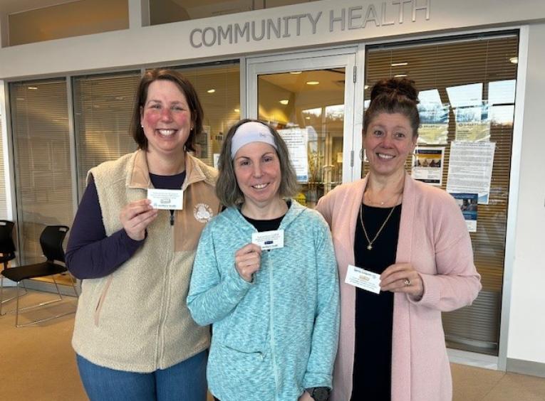 Three women show off their service recognition awards in front of a sign that reads "Community Health"