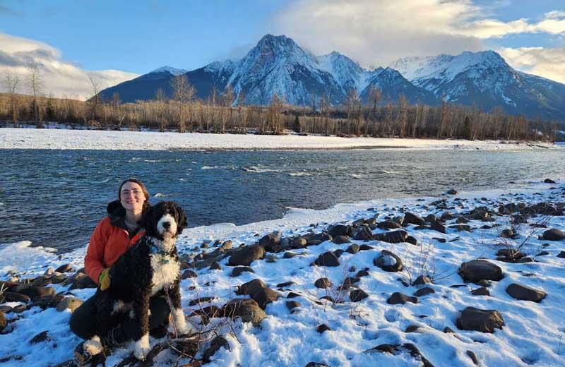 Woman and her dog in winter setting, beside a river with mountains in the background