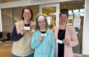 Three women show off their service recognition awards in front of a sign that reads "Community Health"